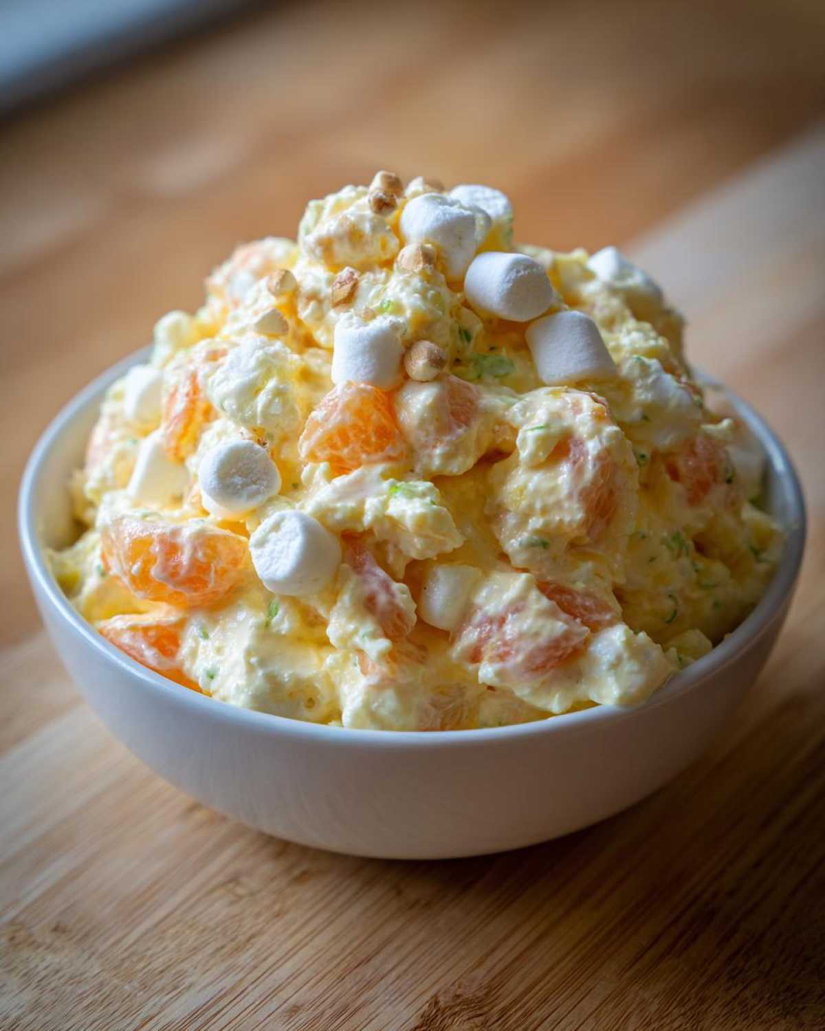 A creamy bowl of Memorial Day : Ambrosia Salad topped with mini marshmallows and nuts.