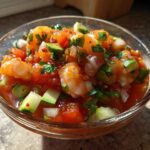 A vibrant glass bowl filled with fresh Mexican shrimp cocktail, featuring plump shrimp, diced tomatoes, avocado, and cilantro.