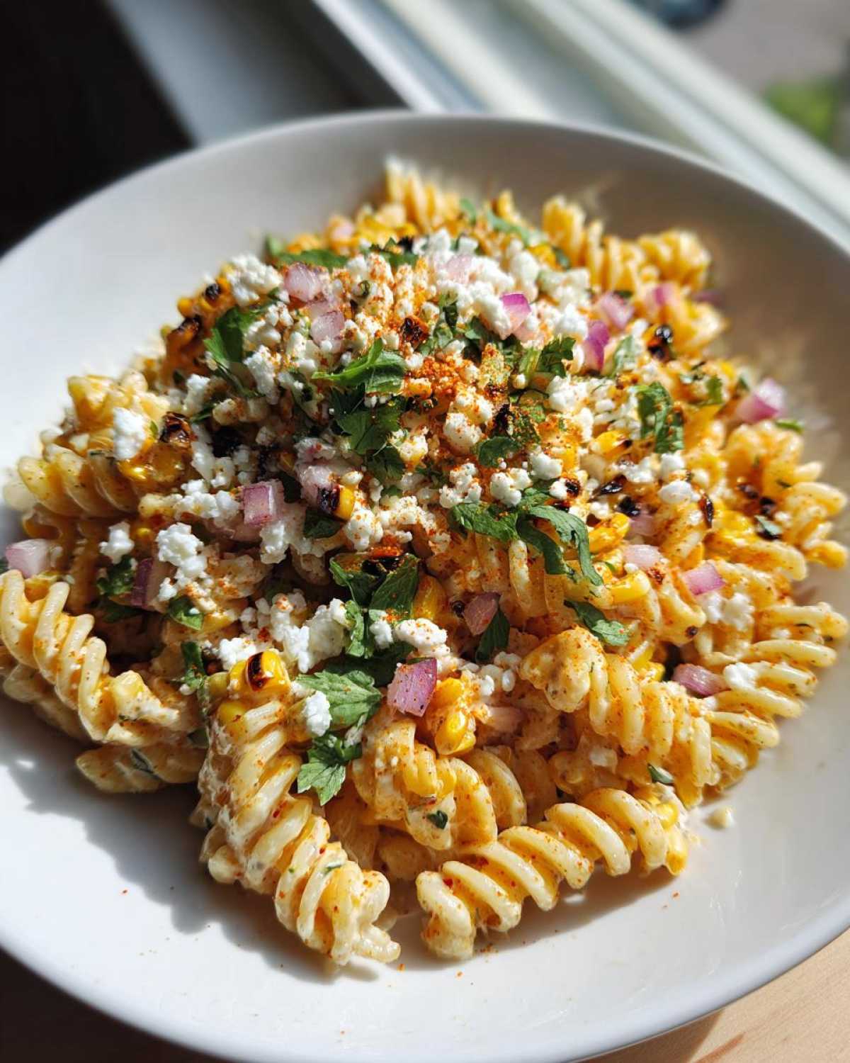 Close-up of a bowl of creamy Mexican Street Corn Pasta Salad topped with cotija cheese, red onion, and cilantro.
