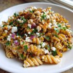 A close-up serving of Mexican Street Corn Pasta Salad featuring fusilli pasta, charred corn, cotija cheese, red onion, and chili powder.
