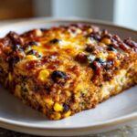 Close-up of a square serving of Mexican Zucchini Casserole topped with melted, browned cheese, corn, and black beans.