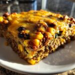A close-up slice of Mexican Zucchini Casserole featuring ground meat, corn, black beans, and a melted cheddar cheese topping.
