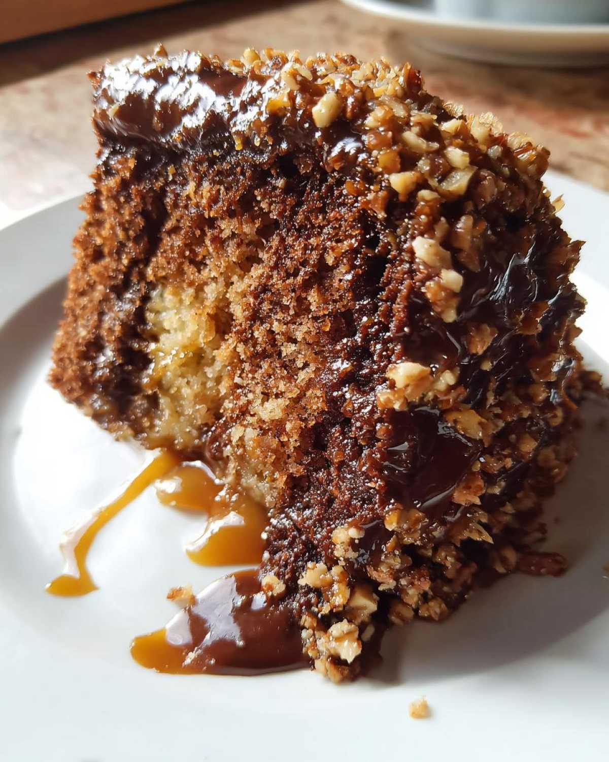 Close-up of a moist slice of german chocolate poke cake topped with gooey caramel sauce and chopped pecans.