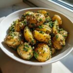 Close-up of a white bowl filled with Mouthwatering French Potato Salad, featuring halved baby potatoes coated in herbs and vinaigrette.