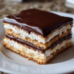 Close-up of a square slice of No-Bake Chocolate Eclair Cake showing layers of graham crackers, cream filling, and chocolate glaze.