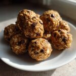 A pile of No-Bake Peanut Butter Energy Bites made with oats and chocolate chips, served on a white plate.