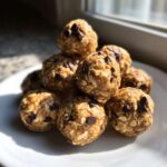 A stack of homemade No-Bake Peanut Butter Energy Bites featuring visible oats and mini chocolate chips, sitting on a white plate.