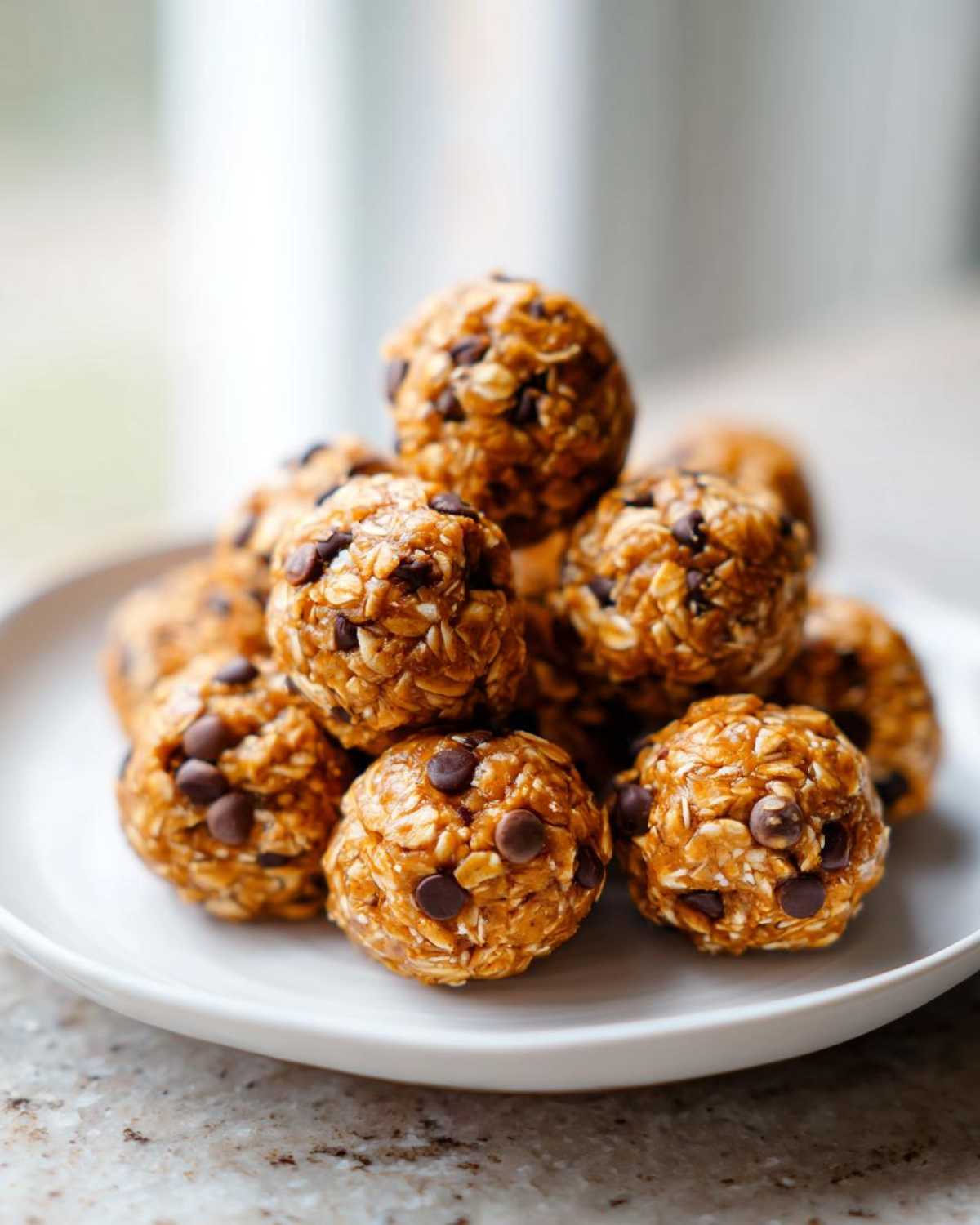 A stack of homemade No-Bake Peanut Butter Energy Bites studded with mini chocolate chips on a white plate.
