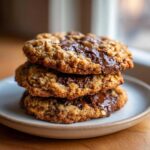 A close-up stack of three freshly baked Oatmeal Chocolate Chip Cookies with melted chocolate.