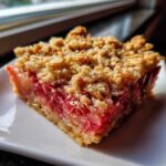 Close-up of a square slice of Old-Fashioned Rhubarb Crunch showing bright pink filling and golden oat topping.