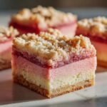 A close-up of a square slice of Ombre Rhubarb Picnic Bars showing three distinct layers: crust, pink filling, and rhubarb topping with a crumb layer.