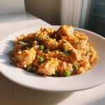 A close-up of creamy rice mixed with chunks of seasoned cajun chicken and bright green peas, garnished with parsley.