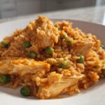 Close-up of a serving of orange-tinted rice mixed with chunks of chicken and bright green peas, representing a Cajun chicken one-pan dinner.