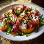 A close-up of a vibrant Peach & Burrata Salad with Prosciutto, arugula, and a balsamic glaze drizzle.