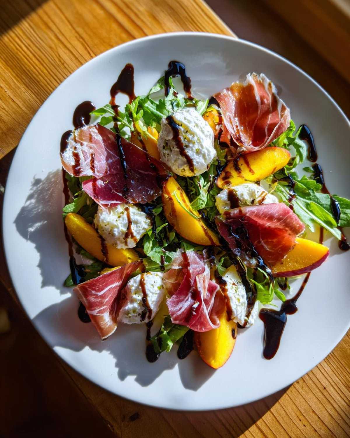 A vibrant Peach & Burrata Salad with Prosciutto served on a white plate, drizzled with balsamic glaze.