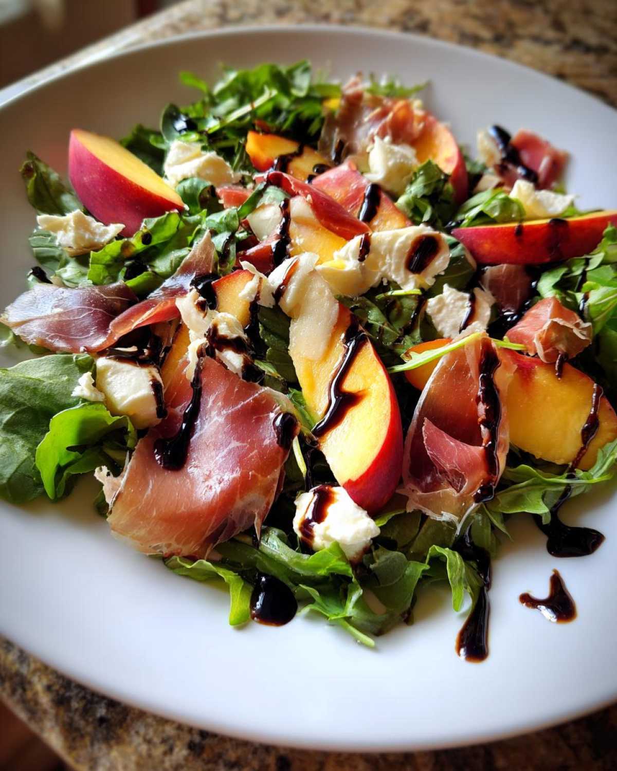 A vibrant close-up of a Peach & Burrata Salad with Prosciutto, arugula, and a balsamic glaze drizzle.