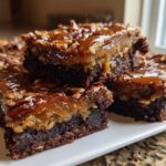 Close-up of several decadent pecan pie brownies stacked, featuring a fudgy base and a gooey caramel pecan topping.