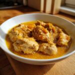 A close-up serving of rich, yellow Persian Rhubarb Chicken with Saffron in a white bowl.
