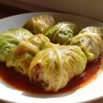A white plate featuring several cooked cabbage rolls nestled in a savory, reddish tomato sauce.