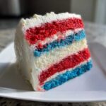 Close-up of a moist slice of Red, White & Blue Layered Flag Cake showing distinct red, white, and blue cake layers with white frosting.