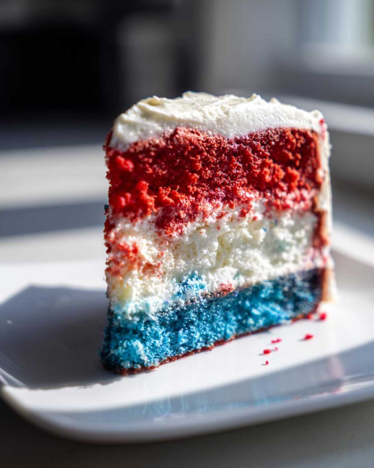A close-up of a slice of Red, White & Blue Layered Flag Cake showing distinct red, white, and blue cake layers with white frosting.