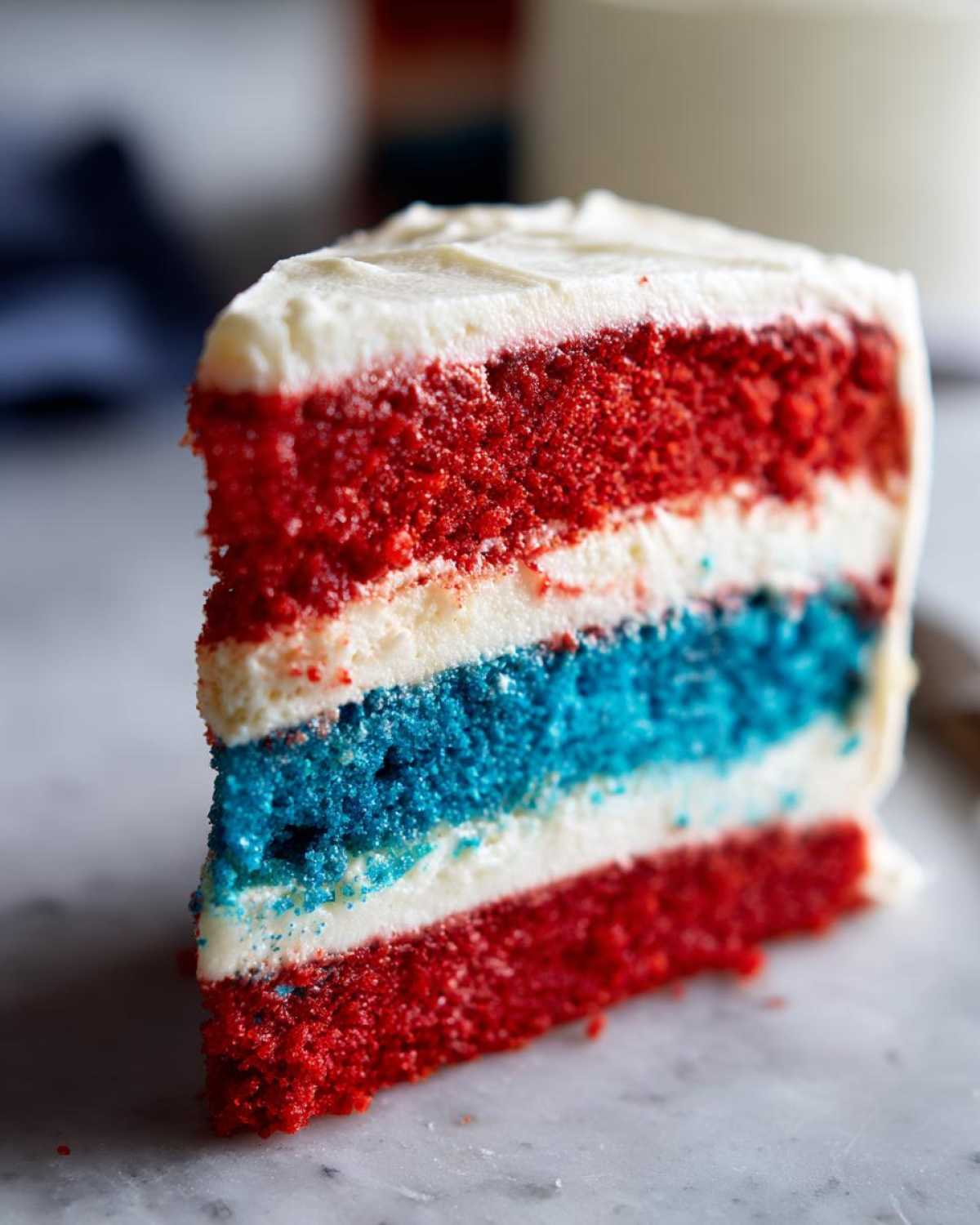 Close-up of a slice of Red, White & Blue Layered Flag Cake showing red, white, and blue cake layers with white frosting.