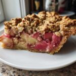 A thick slice of Rhubarb and Apple "Scrunch" Pie showing bright pink rhubarb, apple chunks, and a golden crumble topping on a white plate.