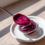 A spoonful of thick, deep magenta Rhubarb and Beetroot Ketchup being lifted from a small glass bowl.
