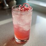 A tall glass filled with a pink, bubbly Rhubarb and Elderflower Gin Fizz, garnished with a rhubarb ribbon.