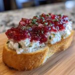A single slice of toasted bread topped with creamy goat cheese and bright red rhubarb compote, garnished with thyme for Rhubarb and Goat Cheese Bruschetta.