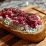 A single piece of Rhubarb and Goat Cheese Bruschetta featuring creamy goat cheese and bright pink rhubarb topping on toasted bread.