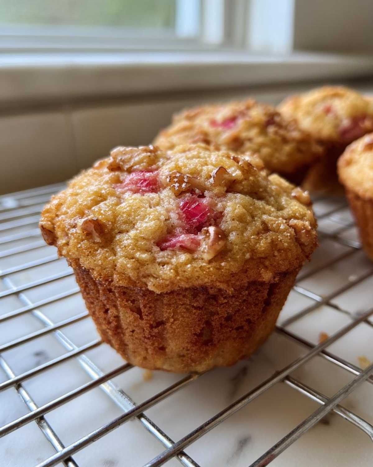 Close-up of a freshly baked Rhubarb and Pecan Muffin with a golden, sugary top cooling on a wire rack.