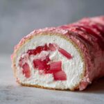 Close-up of a slice of Rhubarb and Rose Meringue Roulade showing pink rhubarb pieces in white cream filling.