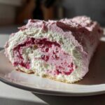 Close-up of a slice of Rhubarb and Rose Meringue Roulade showing the swirl of pink filling and white cream.