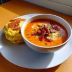 A bowl of vibrant Rhubarb and Tomato Soup with Bacon Omelet served alongside on a white plate.