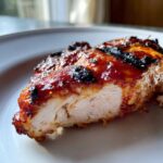 Close-up of juicy grilled chicken breast coated in glossy Rhubarb BBQ Sauce, showing perfectly cooked white meat inside.