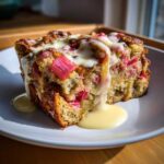 A close-up of a serving of Rhubarb Bread Pudding with Vanilla Custard drizzled generously over the top.
