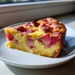 A golden slice of Rhubarb Clafoutis with Stem Ginger showing bright pink rhubarb pieces baked into the custard.
