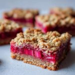 A close-up of one square of Rhubarb Compote Squares showing the bright pink rhubarb filling and crumbly oat topping.