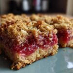 Close-up of two squares of Rhubarb Compote Squares showing a thick, bright red rhubarb filling and crumbly oat topping.