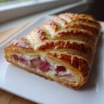 A close-up of a baked Rhubarb Cream Cheese Danish showing the flaky pastry and pink rhubarb filling.
