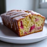 A close-up of a sliced Rhubarb and Earl Grey Tea Loaf, featuring bright pink rhubarb pieces and a white drizzle of icing.
