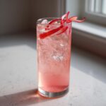 A tall glass filled with a pink, fizzy Rhubarb and Elderflower Gin Fizz, garnished with rhubarb ribbons.