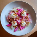 Close-up of a Rhubarb Fennel Salad featuring bright pink rhubarb, white fennel, dollops of roasted ricotta, and candied nuts.