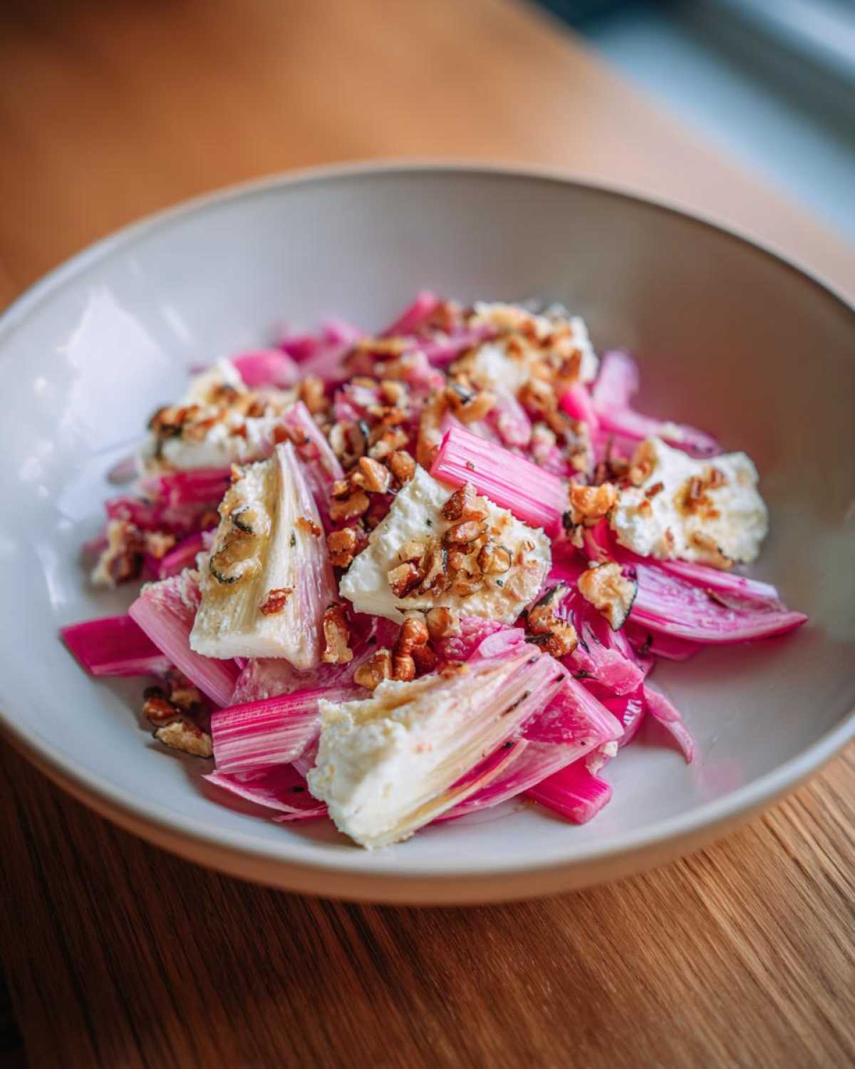 Close-up of a Rhubarb Fennel Salad featuring bright pink rhubarb stalks, roasted ricotta cheese, and toasted nuts.
