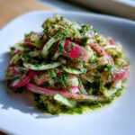Close-up of Rhubarb and Fennel Slaw mixed with bright green chimichurri dressing on a white plate.