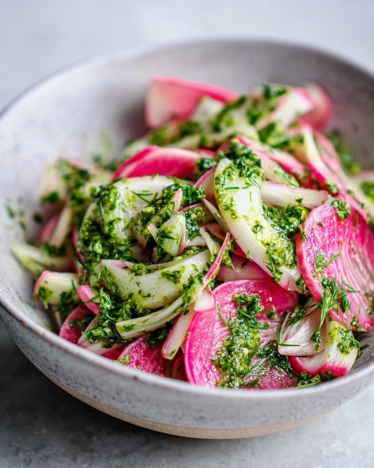 Close-up of vibrant Rhubarb and Fennel Slaw tossed in bright green chimichurri dressing in a ceramic bowl.