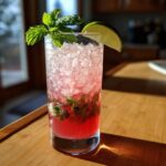 A tall glass filled with a bright pink Rhubarb Mojito with Fresh Mint and Lime, crushed ice, and mint leaves.