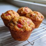 Four golden-brown Rhubarb Muffins with Greek Yogurt cooling on a wire rack near a window.