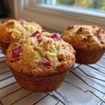 Three golden-brown Rhubarb Muffins with Greek Yogurt cooling on a wire rack near a window.